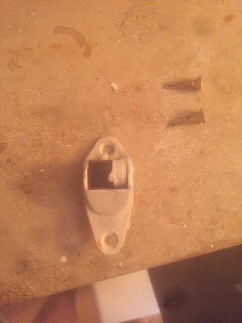 Small white plastic part with metal core on dusty surface; two screws next to it