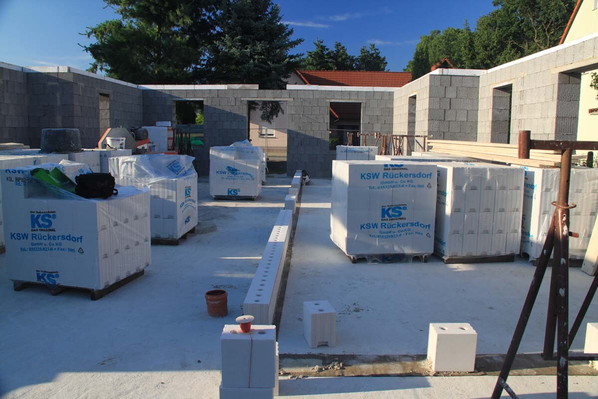 Construction site with stacked concrete blocks on pallets and unfinished walls.