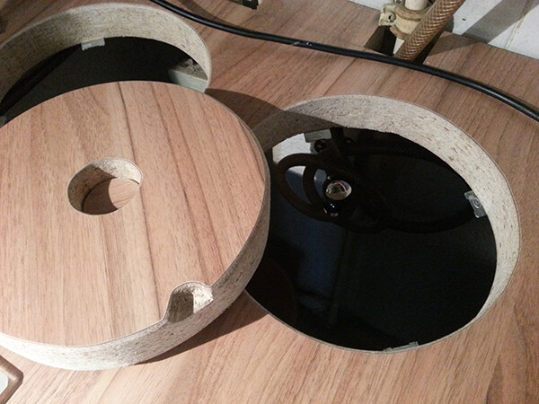 Round wooden lid with cutout lying on wooden floor, cables visible underneath