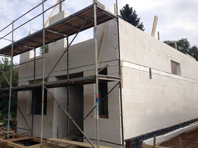 Shell of a house with metal scaffolding; unfinished white masonry walls and window openings.