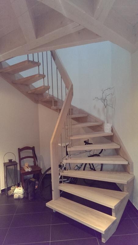 Almost open wooden staircase with railing, interior space, bicycle underneath, vase with branches.