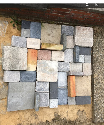 Concrete paving stones stacked side by side on soil next to brick wall