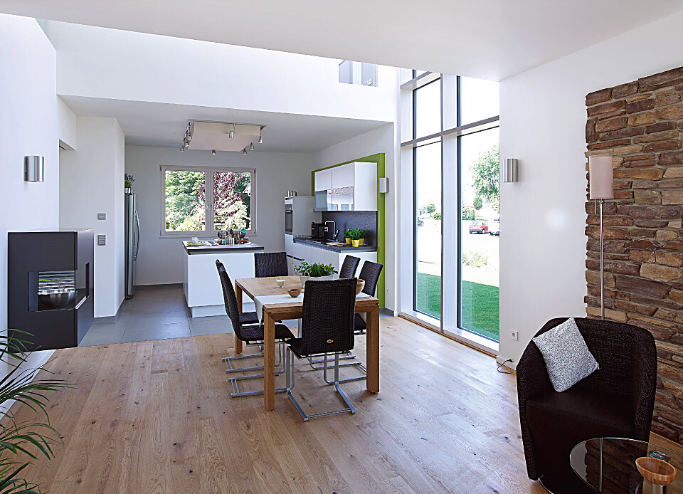 Open modern kitchen-living area with dining table, large windows, and stone wall.