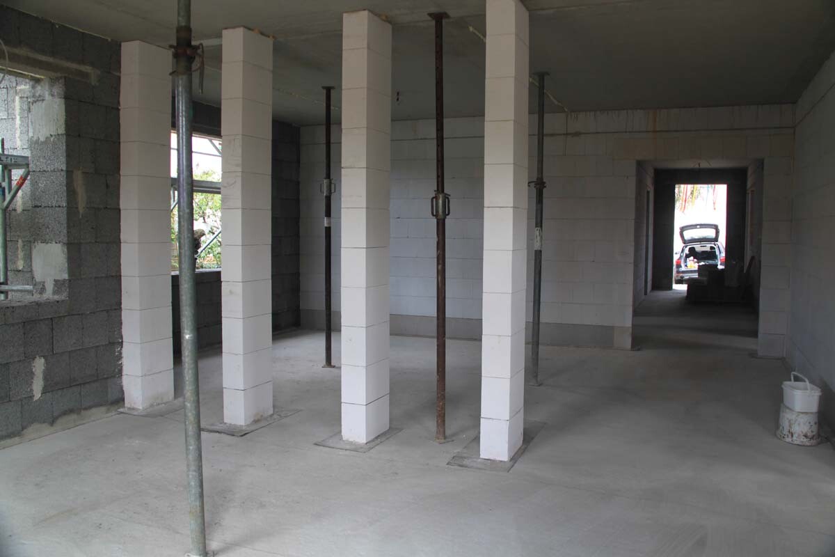 Unfinished interior of a construction site with white columns, steel supports, and a passage to the car outside.