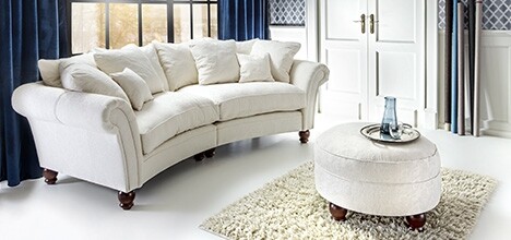 Bright living room with white sofa, round ottoman, rug, and curtains.