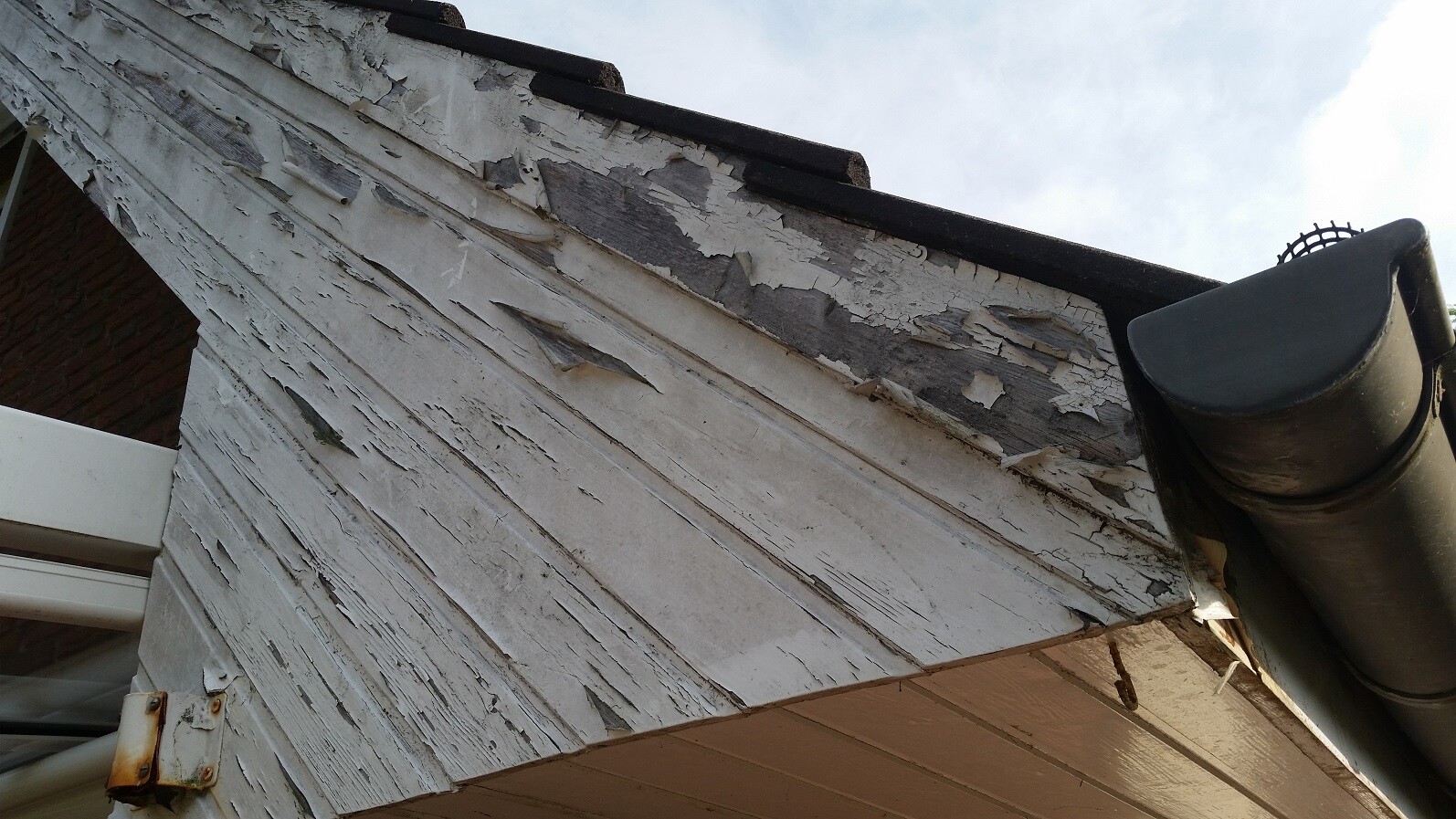Exterior wall with peeling paint and damaged wooden cladding at the eaves