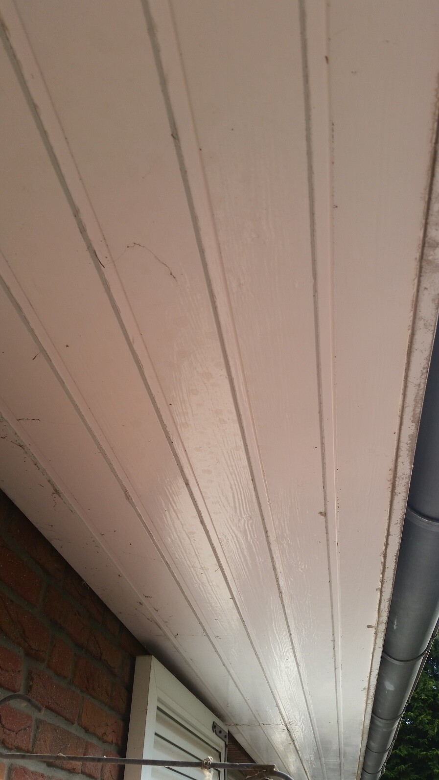Exterior view: white wooden cladding under the roof edge with gutter next to brick wall