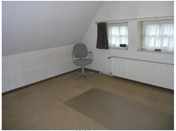 Empty attic room with gray office chair, radiator, and beige carpet