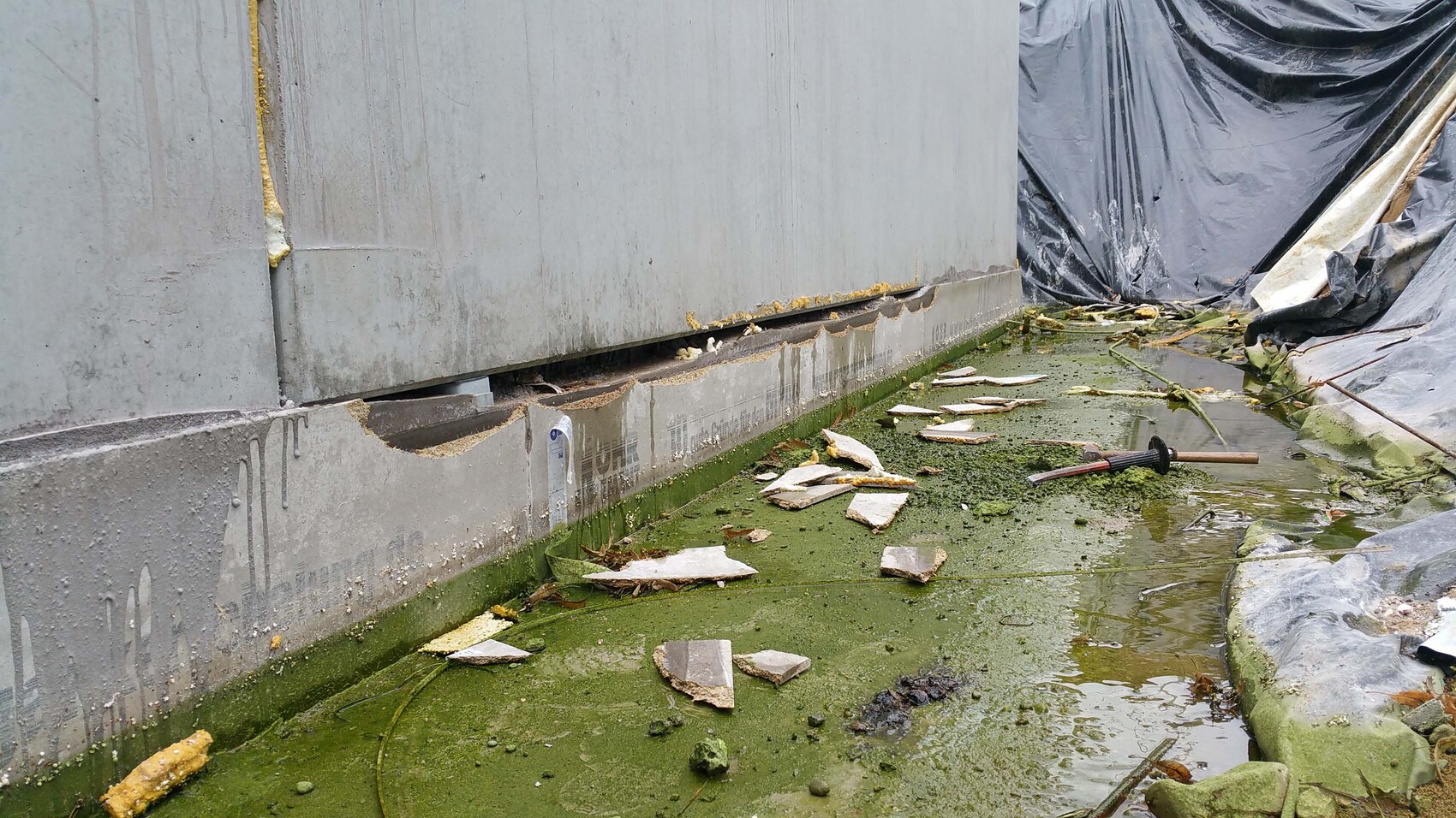 Construction site with damaged foundation, damp ground, and plastic sheeting