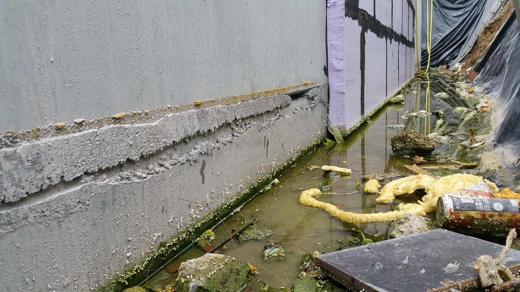Exterior wall insulation at the foundation with water puddle and construction foil during building work