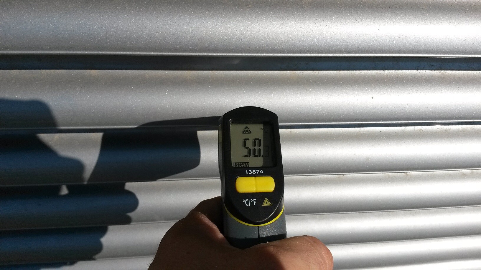 Handliches Infrarot-Thermometer misst Oberflaechentemperatur an Metallblechpaneel.