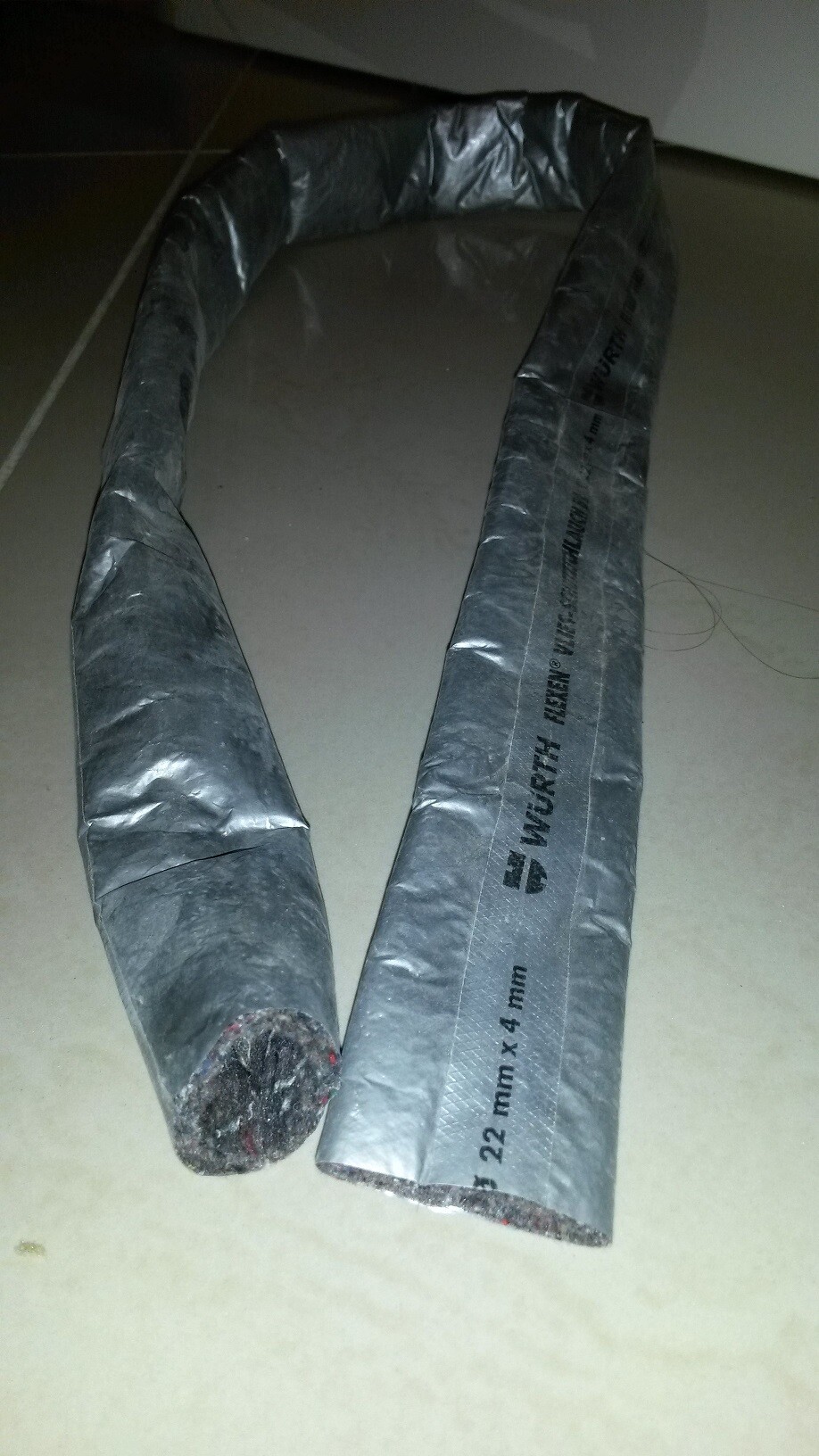 U-förmiges, isoliertes Rohr aus Aluminiumfolie liegt auf Fliesenboden.