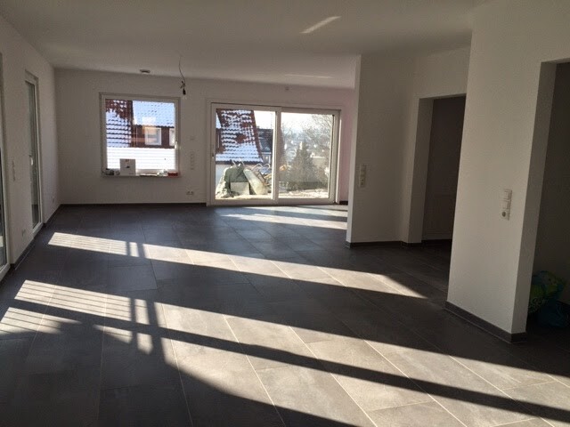 Empty modern living room with large windows, glass doors, and sunlight on tiles.