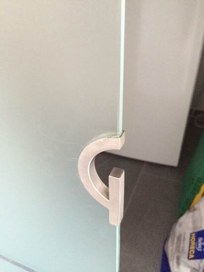 Glass cabinet door with white, C-shaped metal handle; door gap visible.