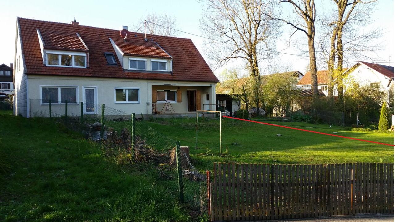 Two-story house with red tiled roof, garden, fence and a red line over the lawn.