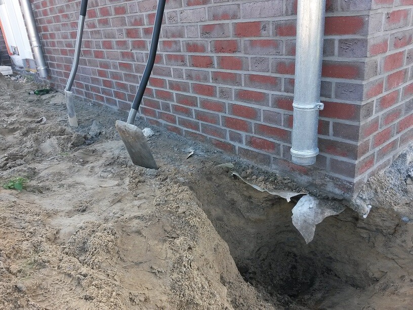 Baugrube am Fundament eines Backsteinhauses, Schaufel im Sand neben der Wand