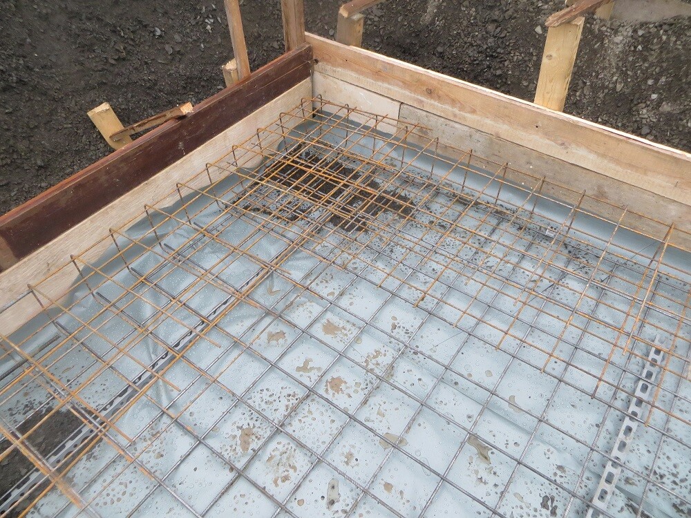 Steel reinforcement mesh lying on a prepared concrete foundation formwork during shell construction.