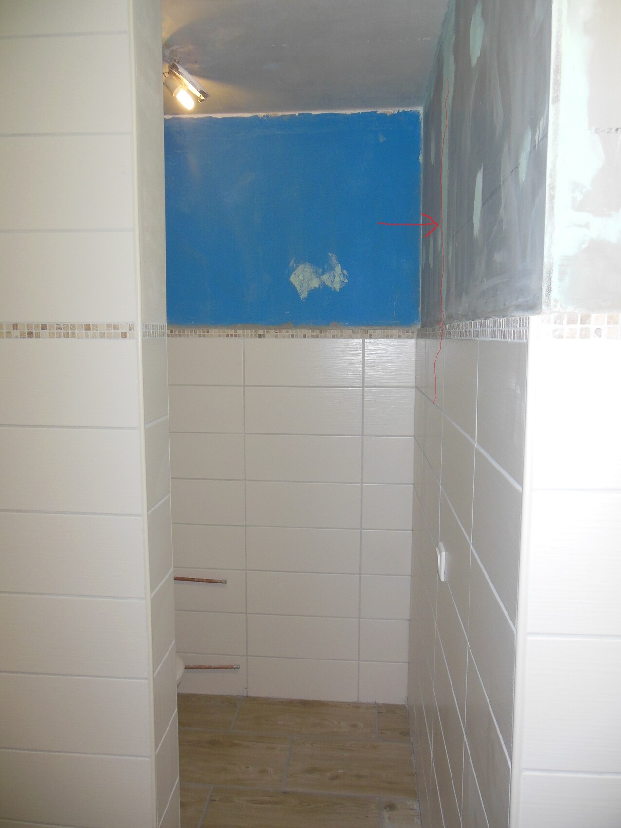 Badezimmer im Bauzustand: weiße Fliesen, blaue Wand, sichtbare Rohbauarbeiten