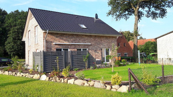 Two-story brick house with dark tiled roof, garden, fence and stone wall.