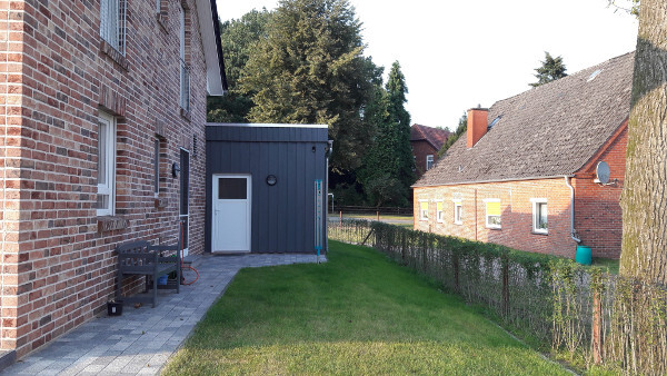 Garden view: brick house on the left, blue shed in the middle, lawn and fence on the right.