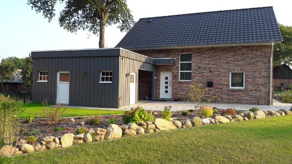 Single-family brick house with gray extension, front garden with stone border and lawn.
