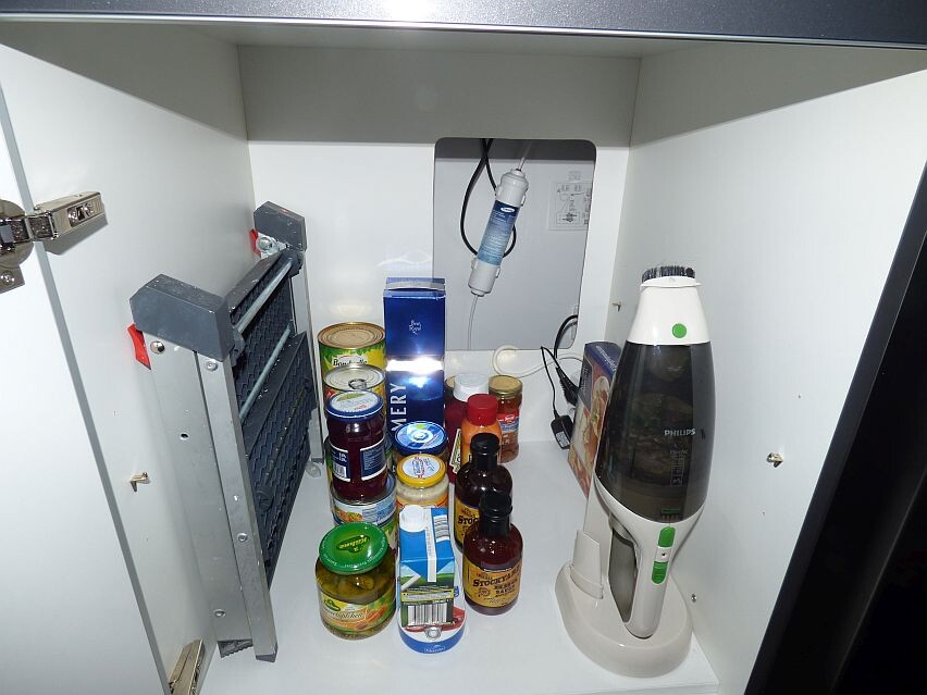 Open kitchen cabinet with supplies, glasses, cans, and a Philips appliance.