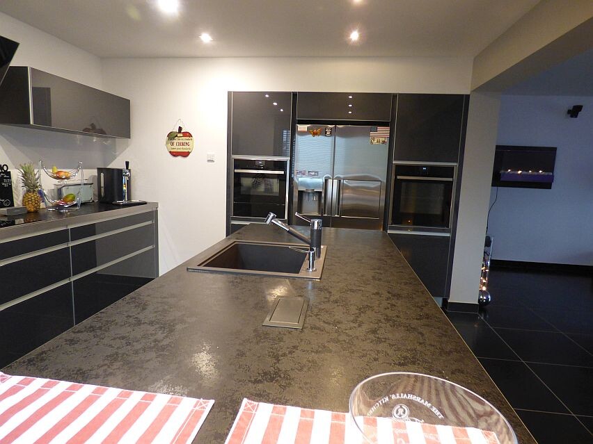 Modern kitchen with island, dark countertop, sink, and built-in ovens.
