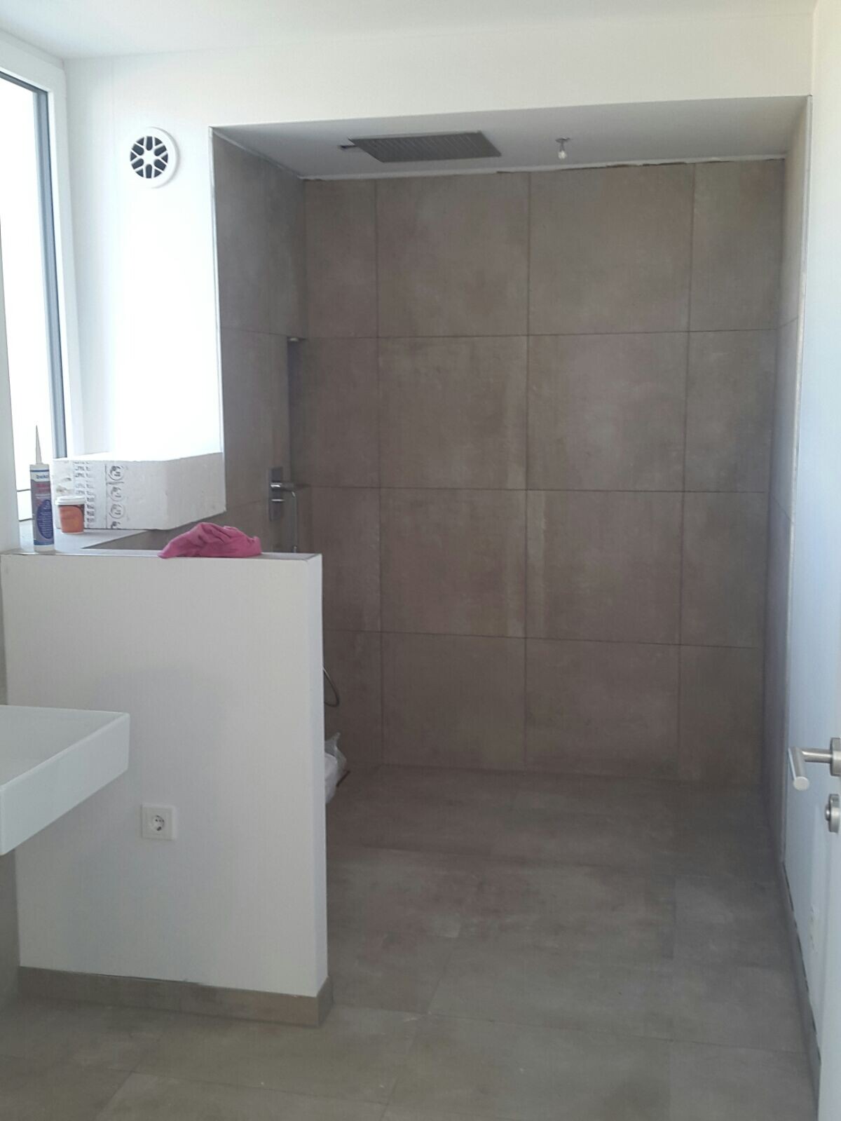 Bathroom with grey tiles, shower niche, white partition wall, window on the left