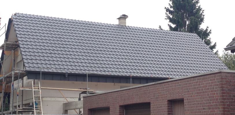 Roof of a house with gray tiles; scaffolding on the left, brick wall below.