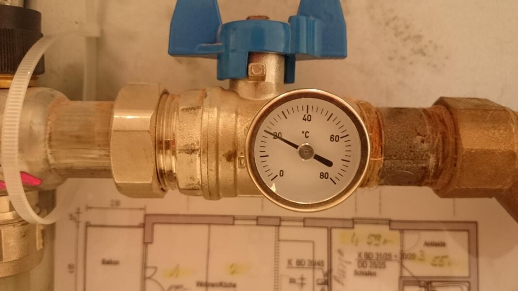 Metallrohrsystem mit blauem Ventilgriff und rundem Temperaturmesser (°C) am Anschluss.