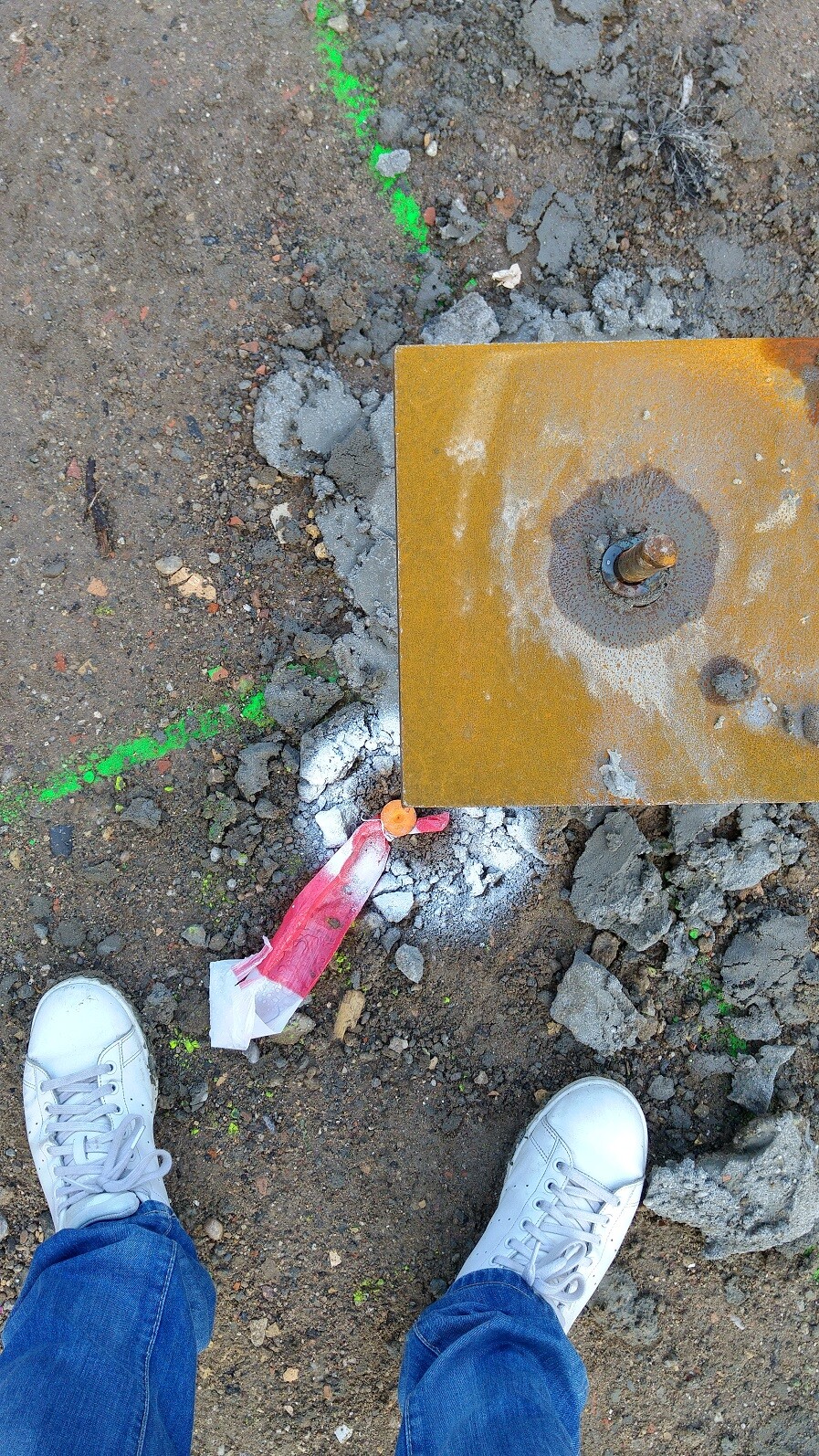Blick auf Fundamentplatte mit Rost, Baugelände, grüne Markierung und Schuhe im Vordergrund