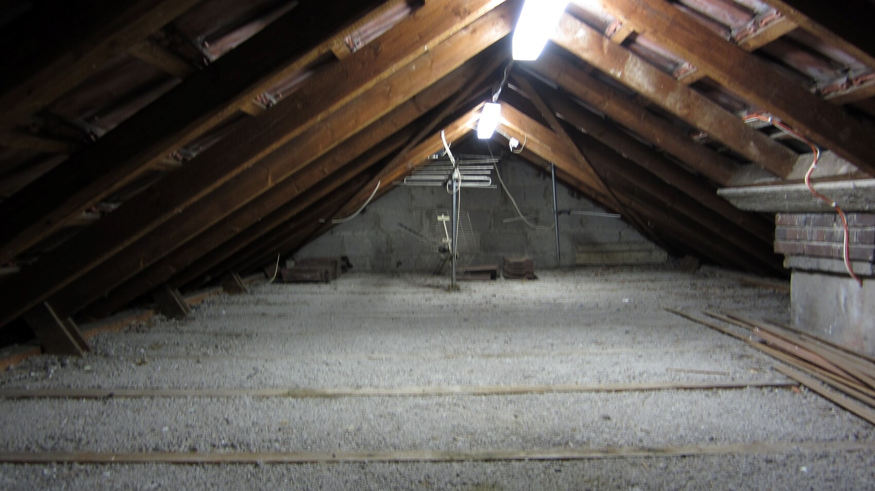 Dachboden mit sichtbarem Holz-Dachstuhl, Deckenbalken, lose Bauholz und zentrale Leuchte