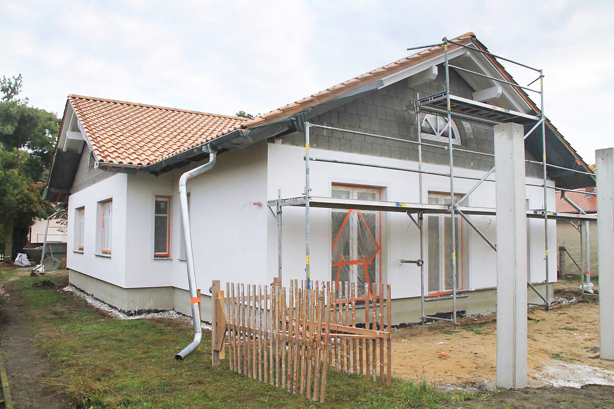 Neubau eines Einfamilienhauses mit Gerüst, weißer Fassade und rotem Ziegeldach.