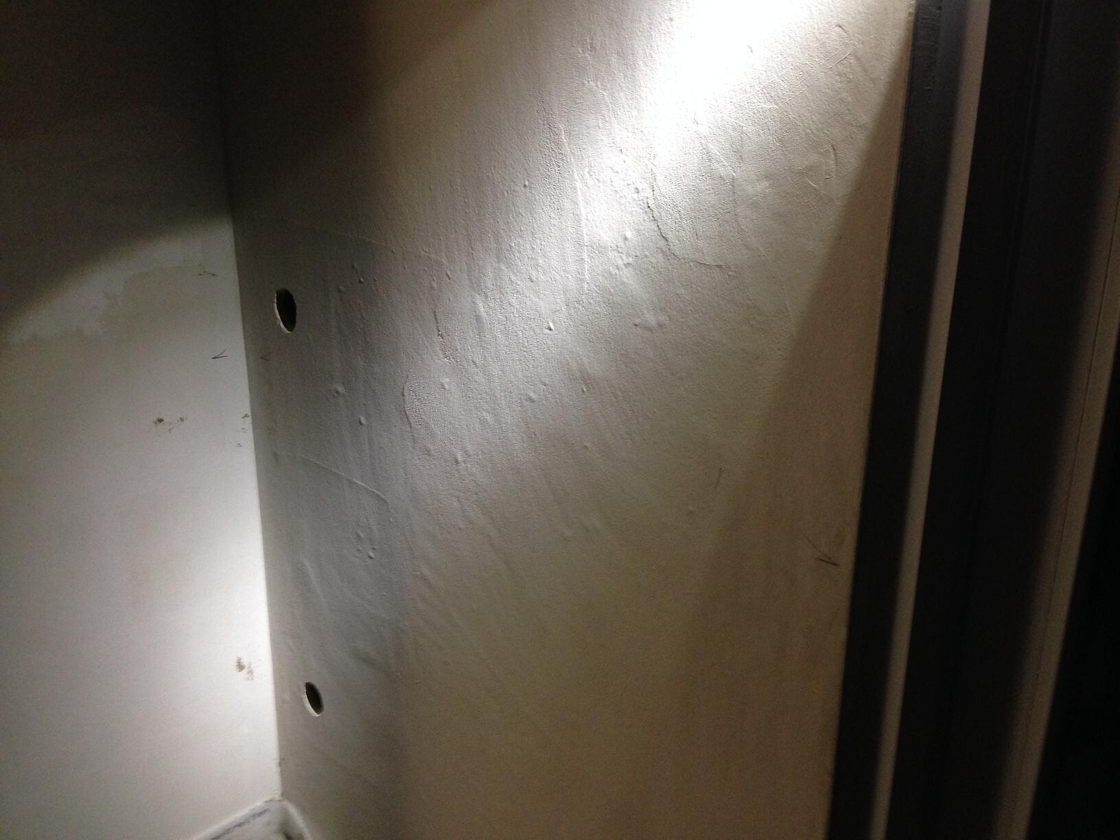 Unfinished interior wall with drill holes and rough plaster
