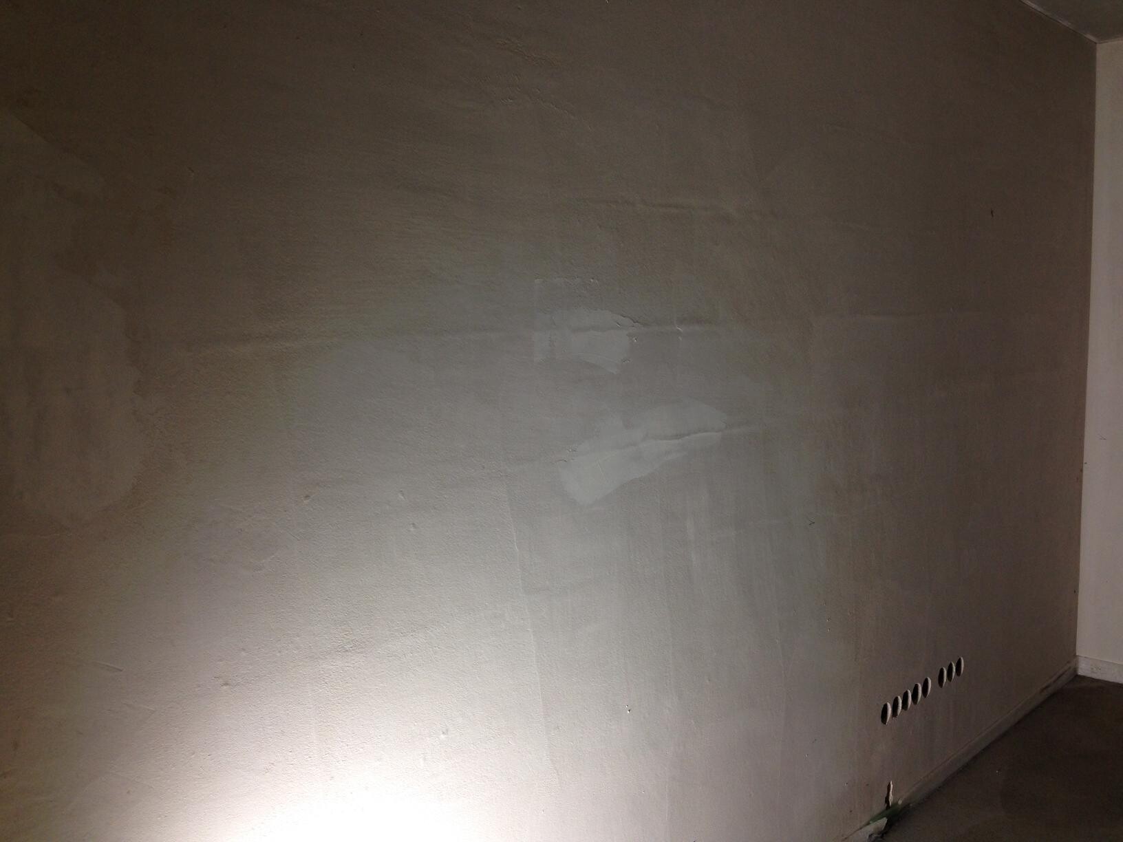 Unplastered interior wall in the shell construction with uneven surface and ventilation openings at the base.