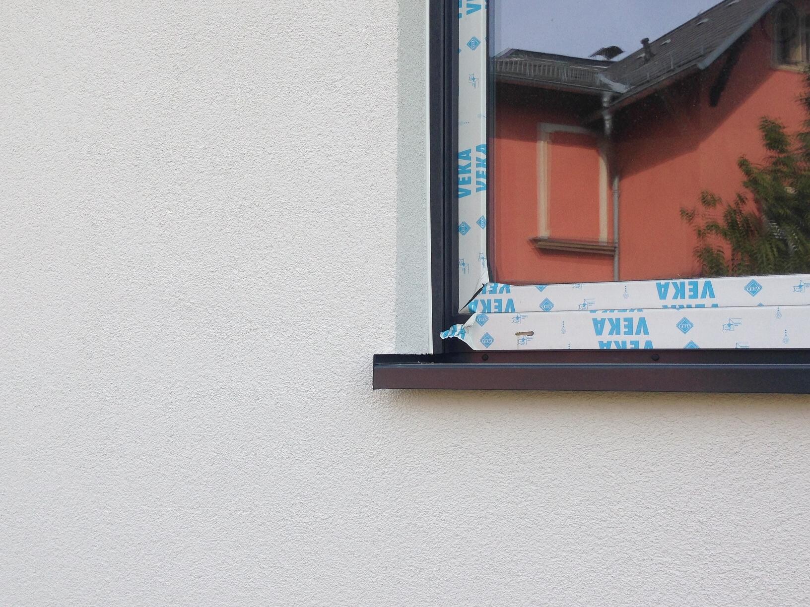 Exterior wall with newly installed window frame and protective foil, red neighboring house in the background