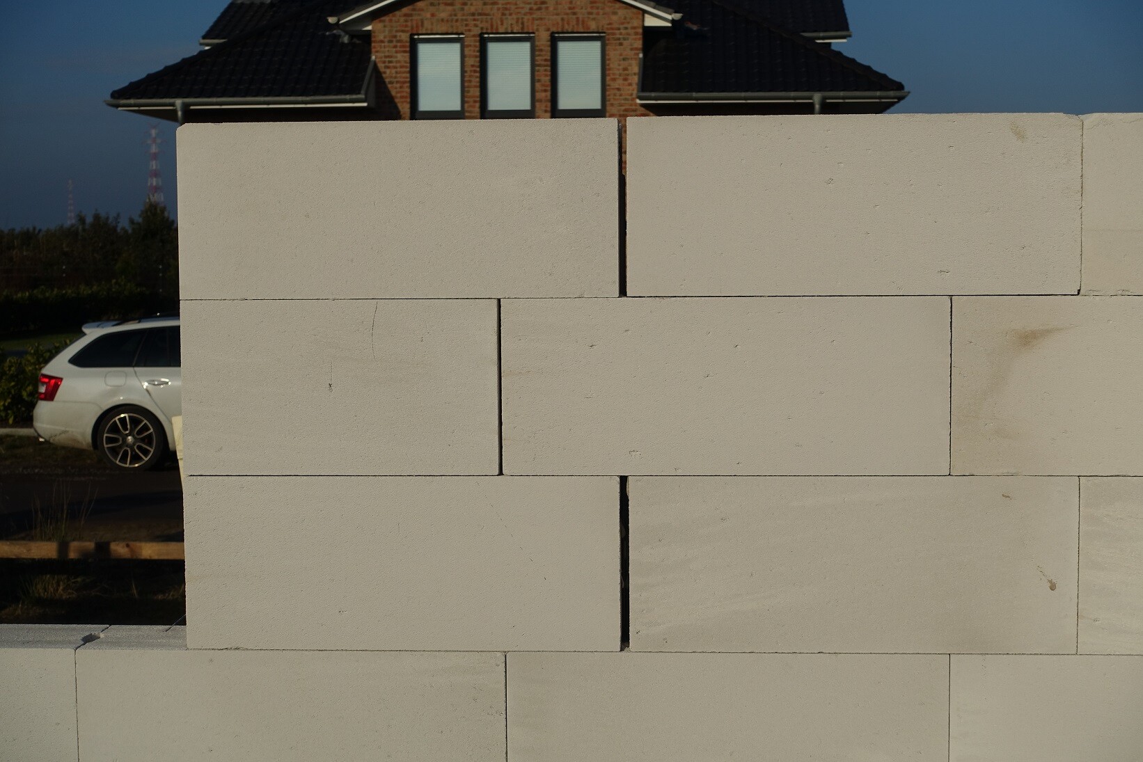 Grosse Betonblockwand im Rohbau vor einem Wohnhaus, links steht ein weisses Auto.
