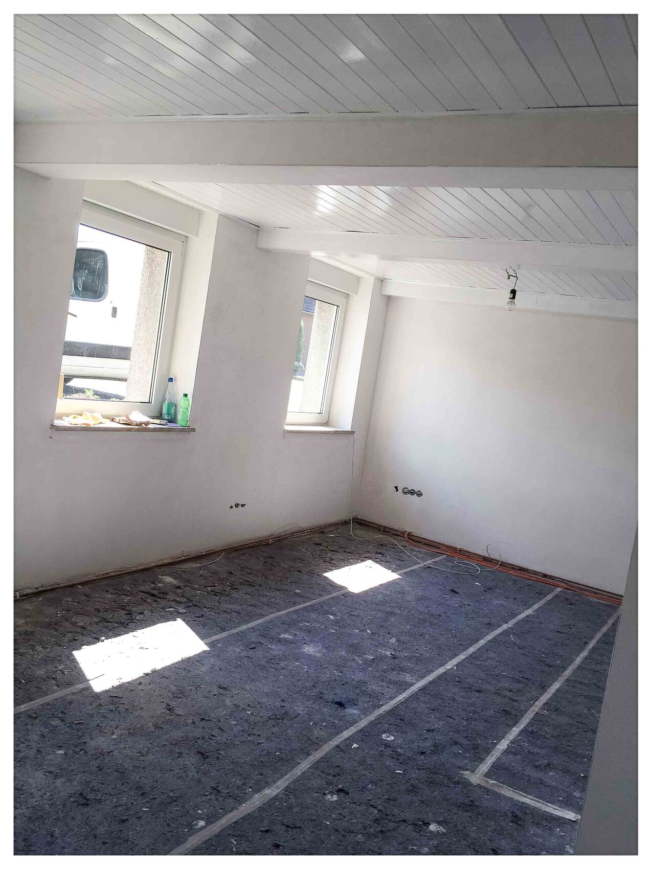 Empty renovation room with white walls, ceiling cladding, window fronts, and leftover cables.