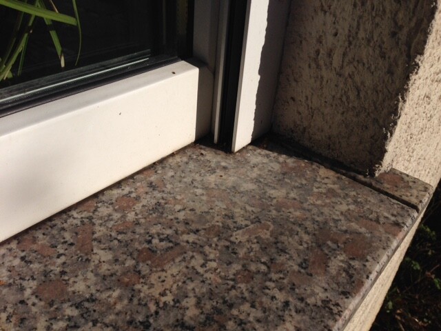 Exterior granite windowsill next to door frame, stone texture visible