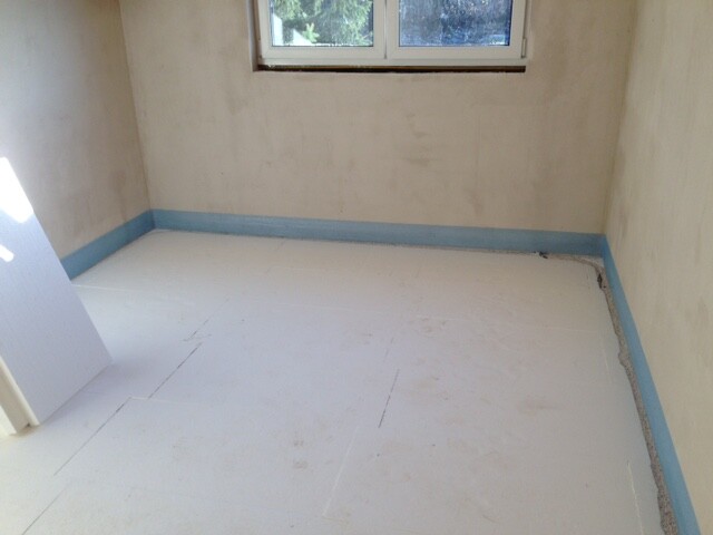 Small unfinished bathroom with window, white floor, and blue floor edging.