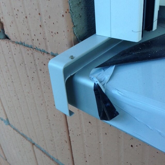 Close-up of a metal window frame with tape on a brick wall.