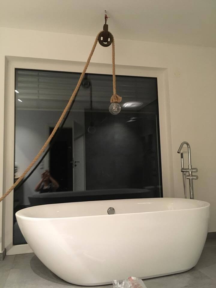 Modern bathtub: freestanding white bathtub in front of a window; a cord with a light bulb hangs above.