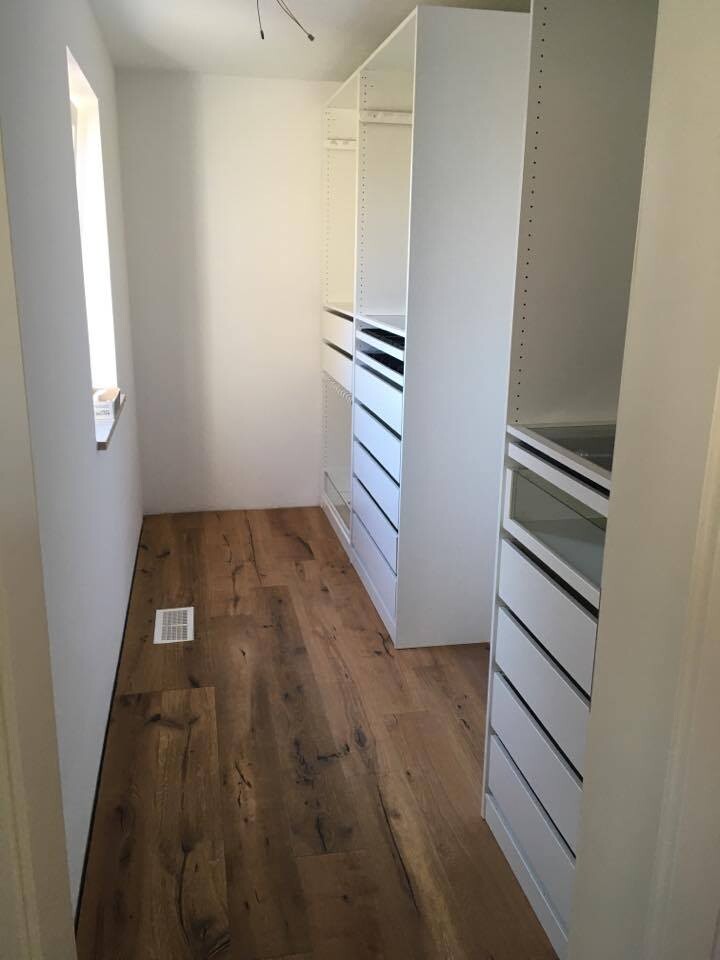 Bright, narrow dressing area with white shelves, drawers, and wood flooring.