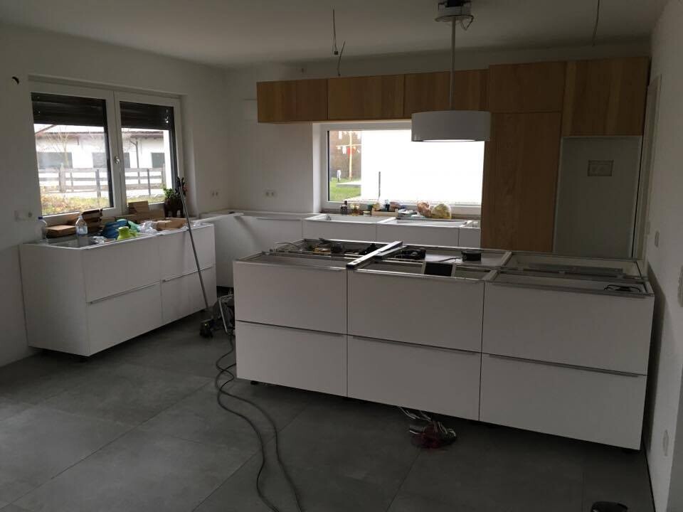 Modern white kitchen under construction: island in the middle, wooden upper cabinets, tools on the countertop.