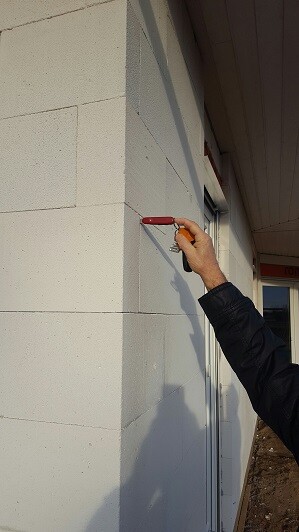 Person malt mit Farbroller eine rote Linie auf eine helle Außenwand