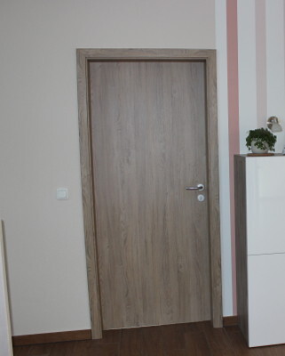 Interior entrance door with wood finish in hallway with wooden floor and white sideboard