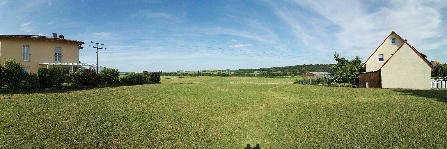 Rural plot with two houses, green lawn and wide sky