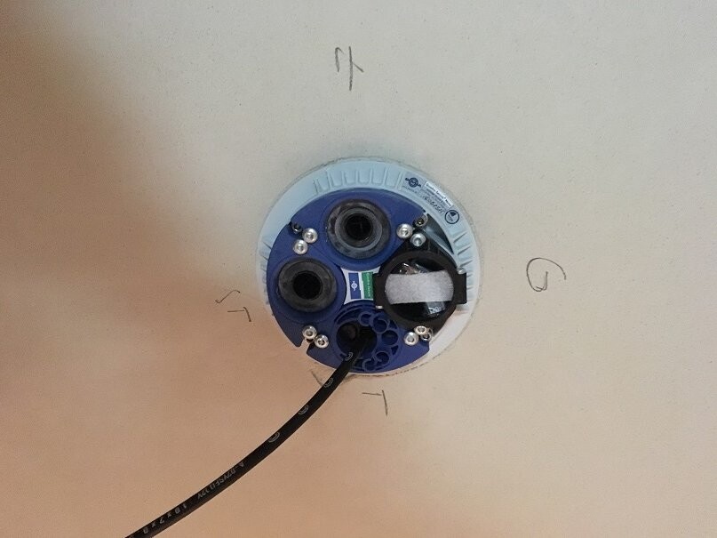 Recessed ceiling spotlight with blue mounting base and visible cables on building substrate.
