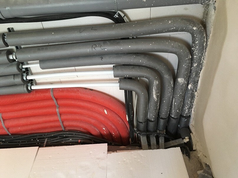 Several gray pipes with bends and a red flexible hose in a technical room.