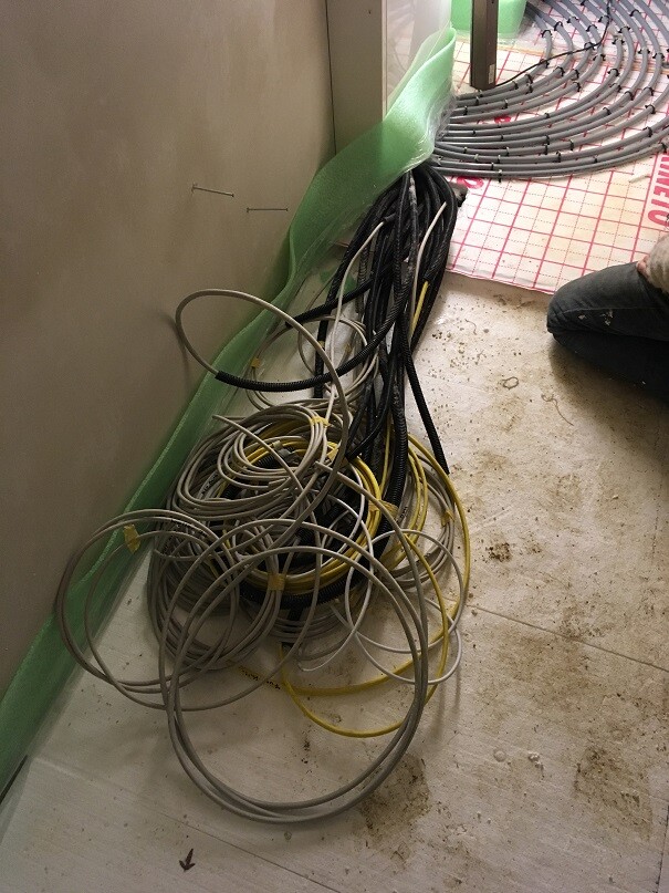 Tangled cable bundles on the construction floor next to a wall.